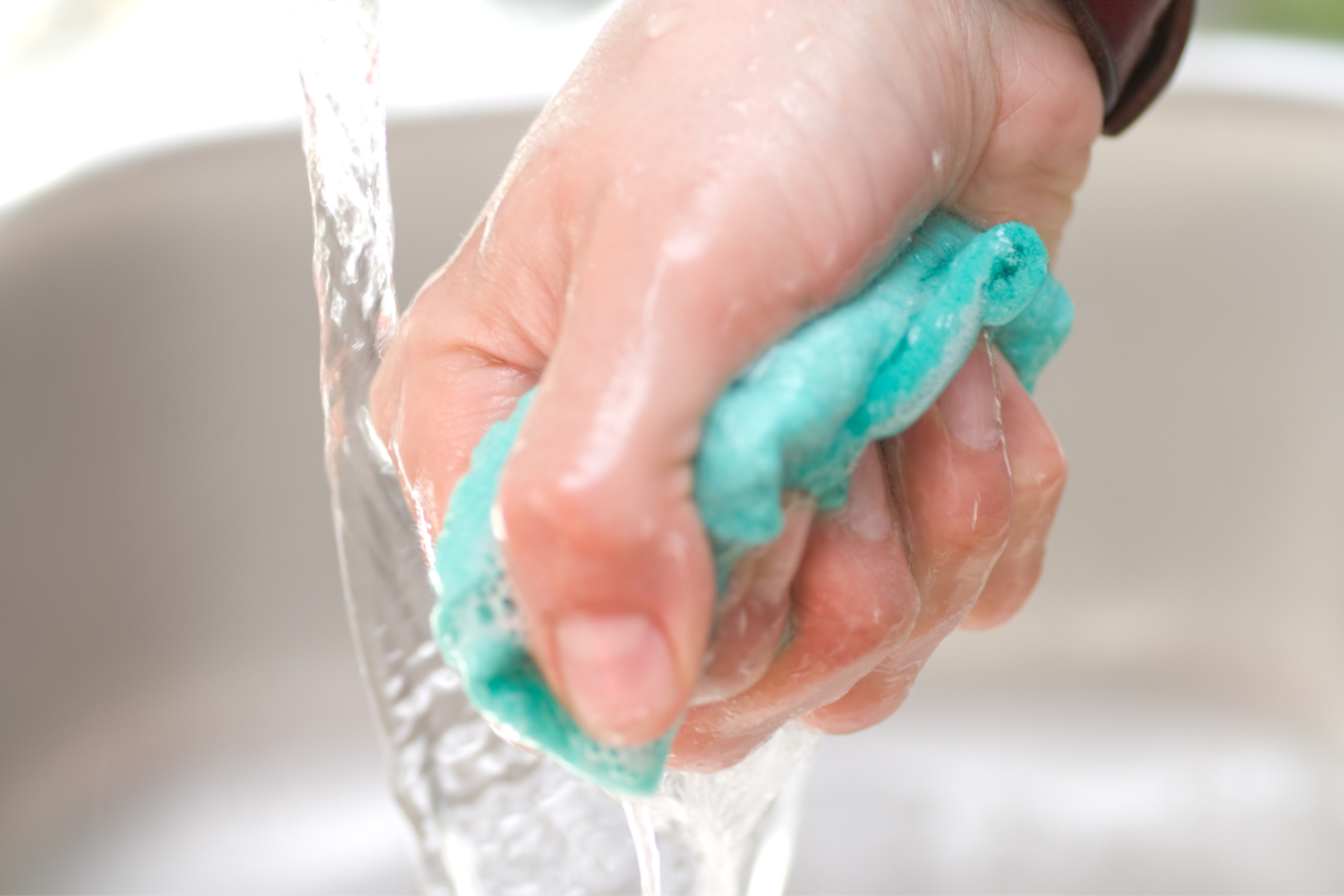 Bayeta azul de microfibra siendo escurrida con jabón, proceso de limpieza con Sanytol