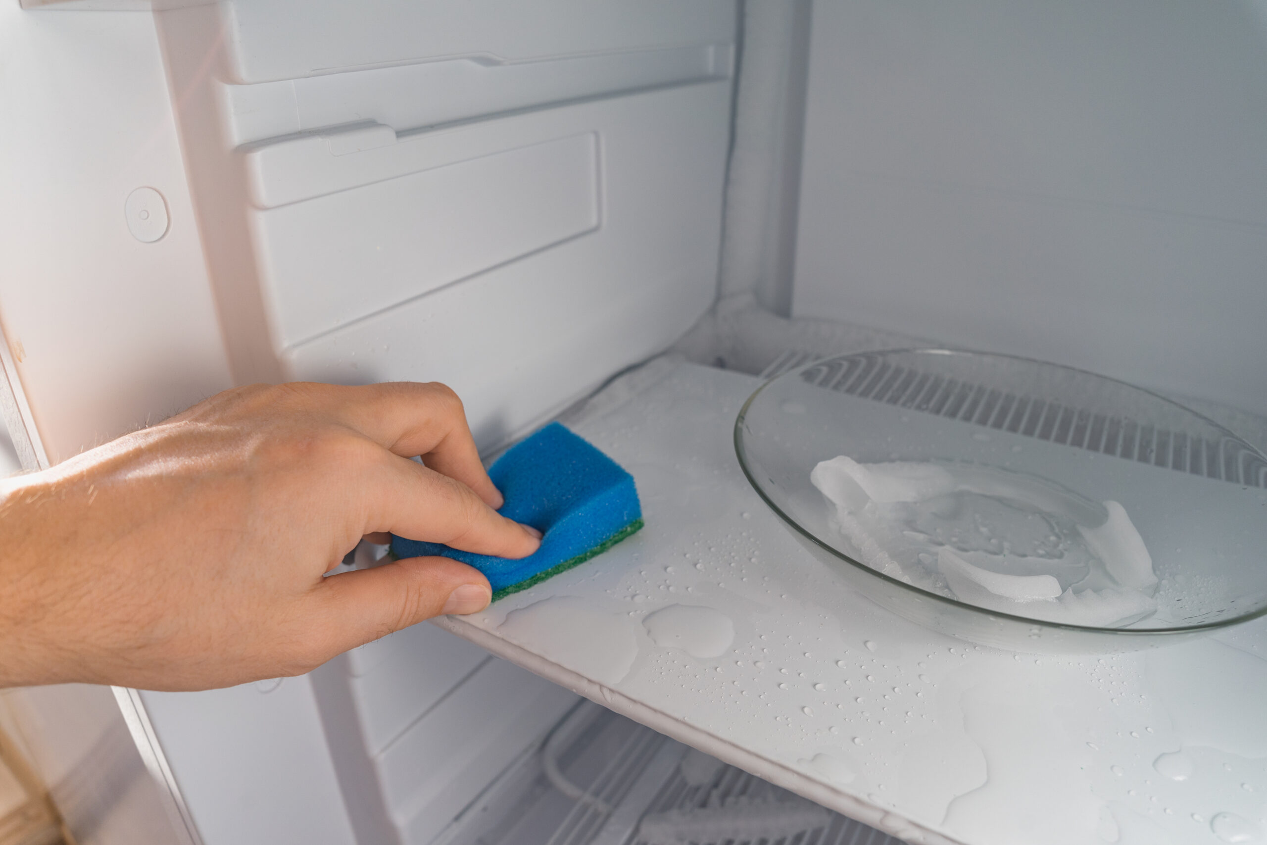 Persona eliminando el mal olor del congelador utilizando una bayeta y productos de limpieza