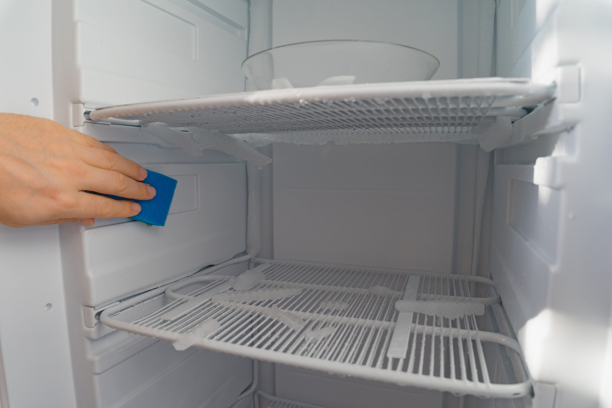 Persona continuando la limpieza del congelador con bayeta azul para remover olores
