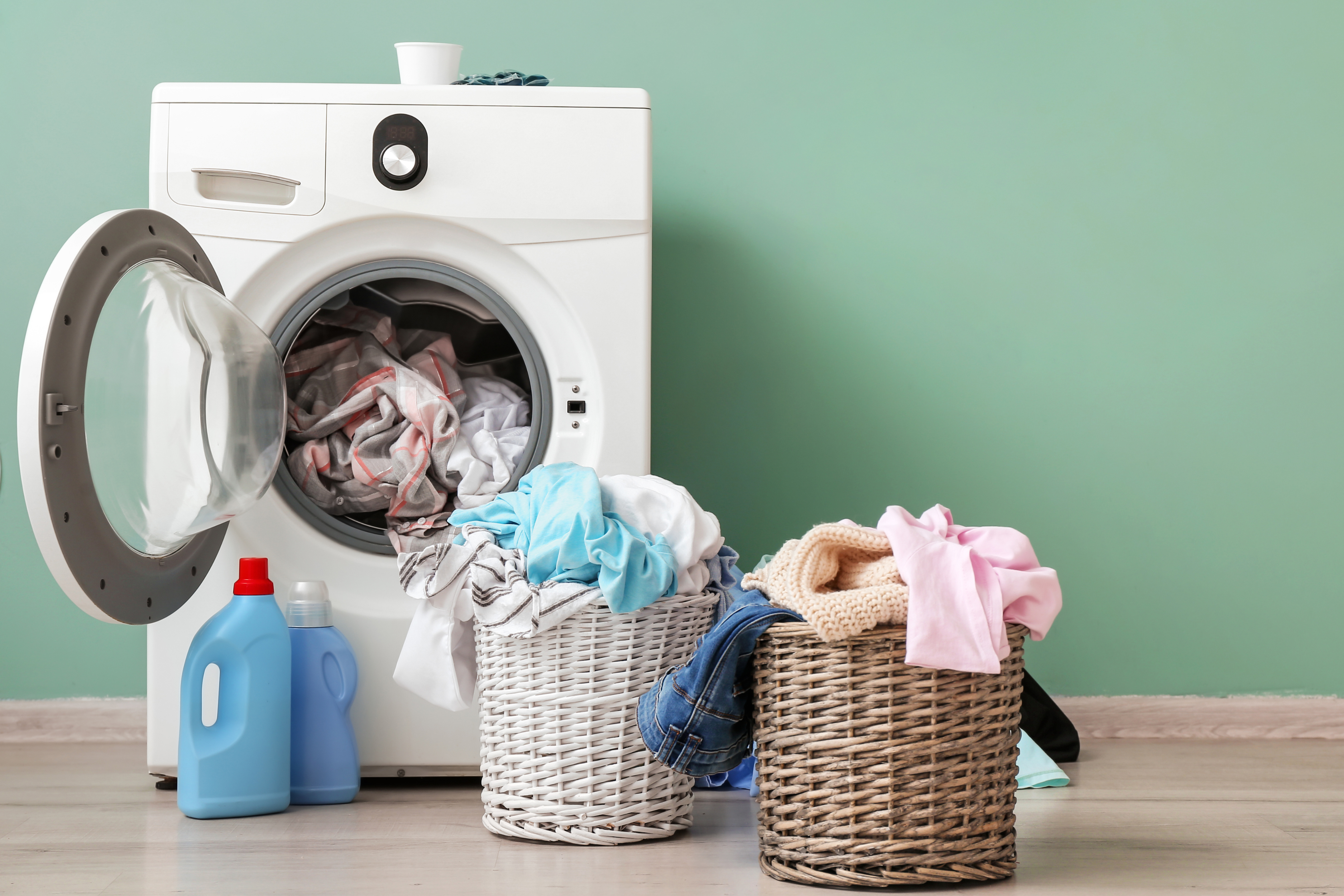 Lavadora junto a un cesto de ropa, resaltando la importancia de secar completamente las prendas para evitar la humedad y el crecimiento de hongos